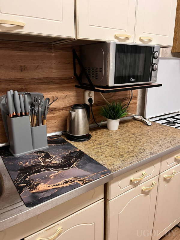 Органайзер с приборами, мраморная подставка, электрический чайник, горшок с зеленью и настенная микроволновка «Midea» над деревянной панелью.