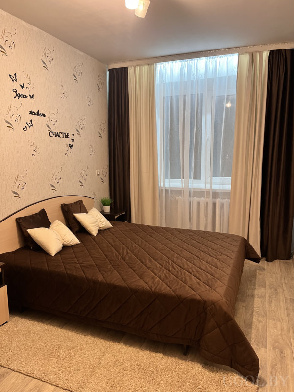 Комната с текстурными обоями, растением на тумбочке и большими окнами с плотными шторами.