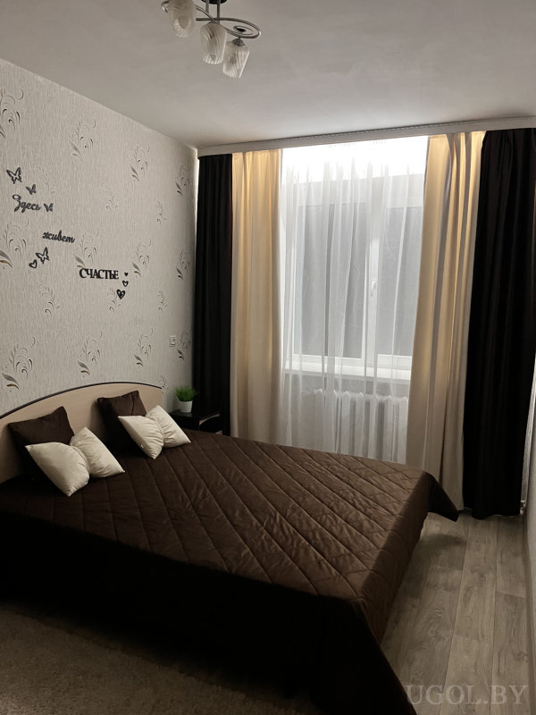 Интерьер с теплым освещением, растением у кровати и декоративной надписью на стене.