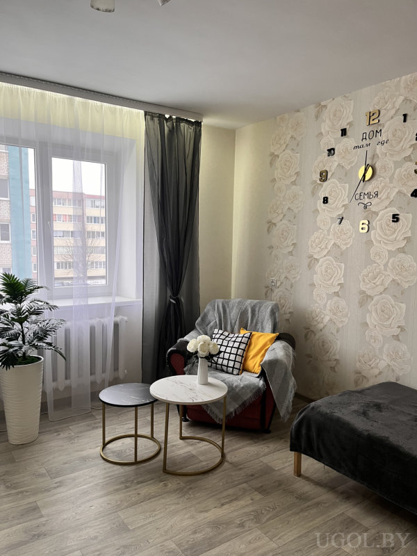 Уютный уголок с красным креслом, мраморными столиками и настенными часами с текстом.