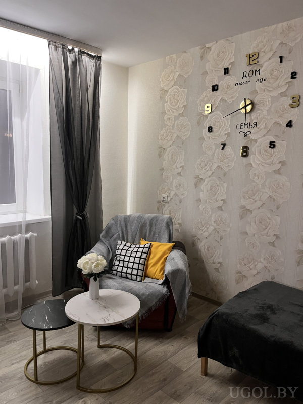 Гостиная с декоративными часами, цветами и стильной мебелью в нейтральных тонах.