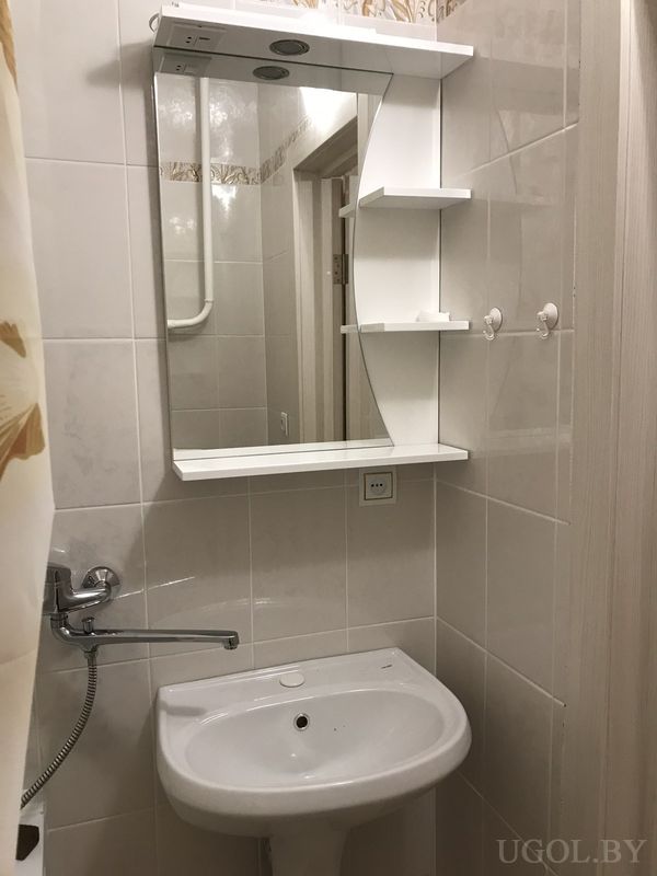 Компактная ванная с зеркальным шкафом, белой раковиной, настенным смесителем и душевой занавеской с цветочным узором.