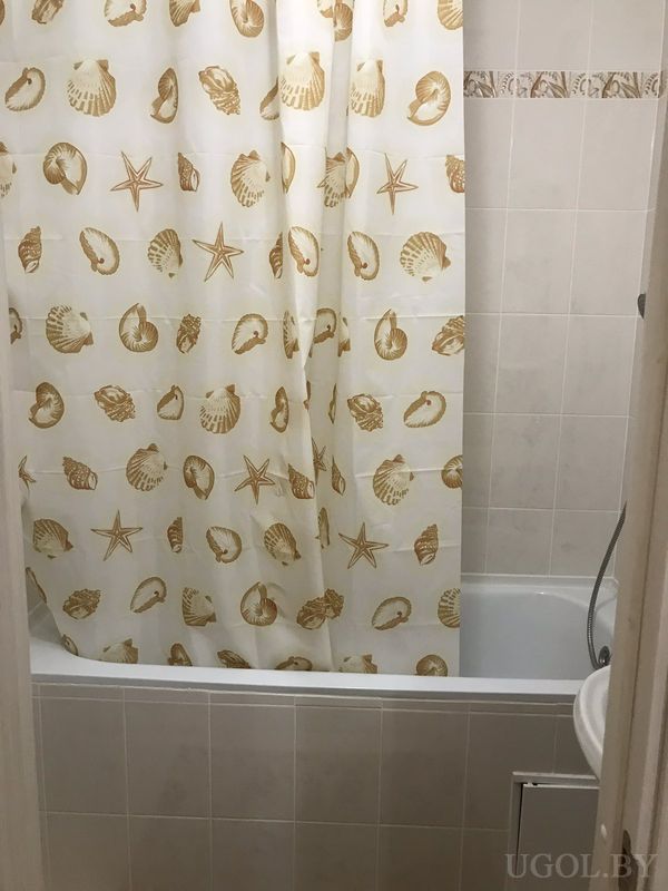 Ванная с белой ванной, занавеской с ракушками и звёздами, светлой плиткой и ручным душем.