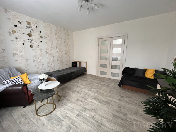 Комната с креслом, диваном и тахтой, оформленная в светлых тонах с настенными часами.