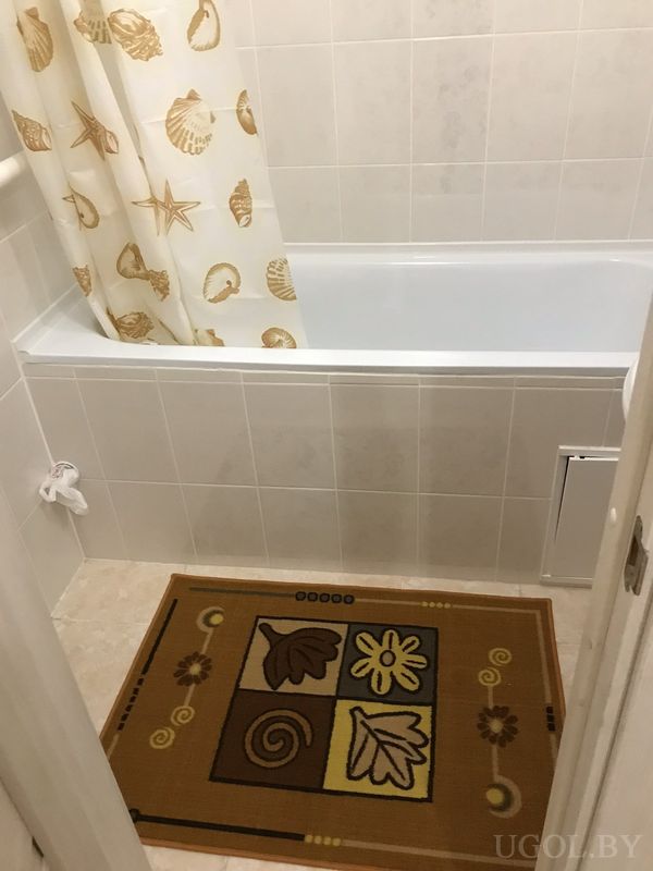 Чистая ванная с белой ванной, занавеской с морским принтом, декоративным ковриком и полотенцем на крючке.