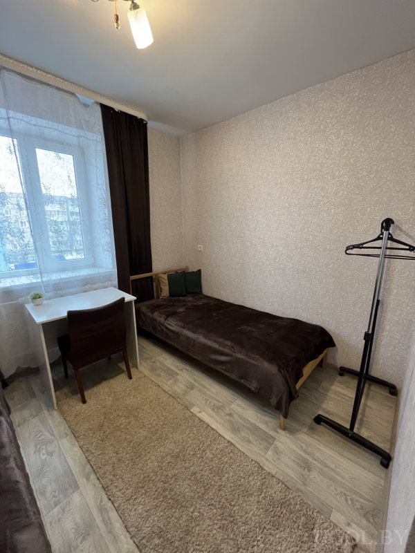 Интерьер с рабочим столом, зеленой подушкой и черной вешалкой.