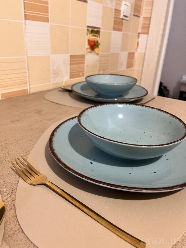 Стол с голубыми тарелками, золотыми приборами и плиткой с фруктовыми мотивами.