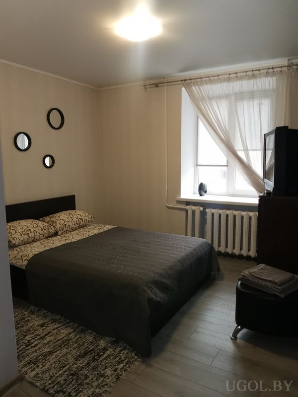 Современная спальня с кроватью в тёмном изголовье, серым покрывалом, декоративными круглыми зеркалами на стене и телевизором на тумбе.