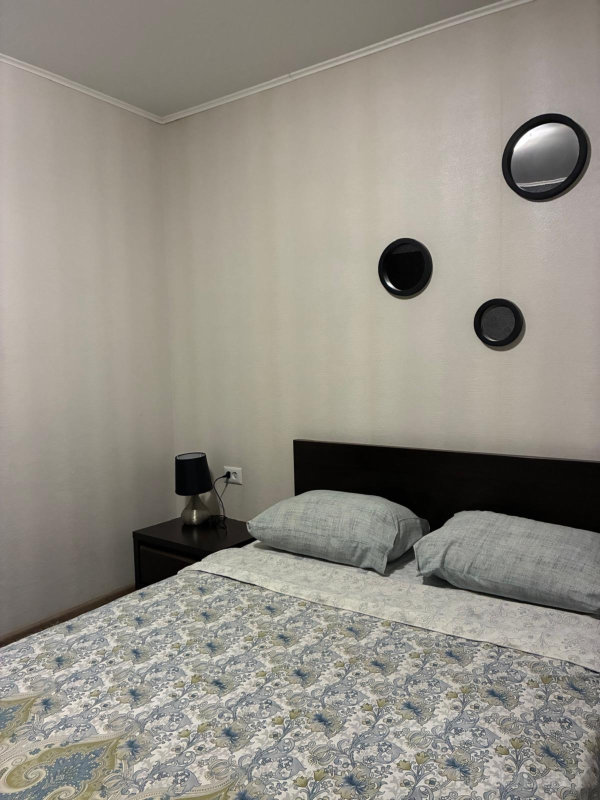 Спальня с деревянной мебелью, серыми подушками и асимметрично размещёнными зеркалами над изголовьем.