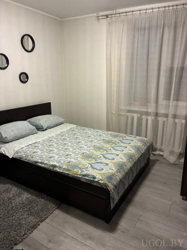 Кровать с сине-зелёным текстилем, коврик у кровати и четыре круглых зеркала на стене.