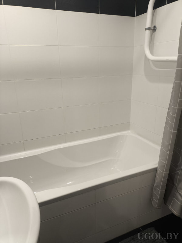 Белая ванна, душевой шланг и геометрическая штора на фоне бело-чёрной отделки.