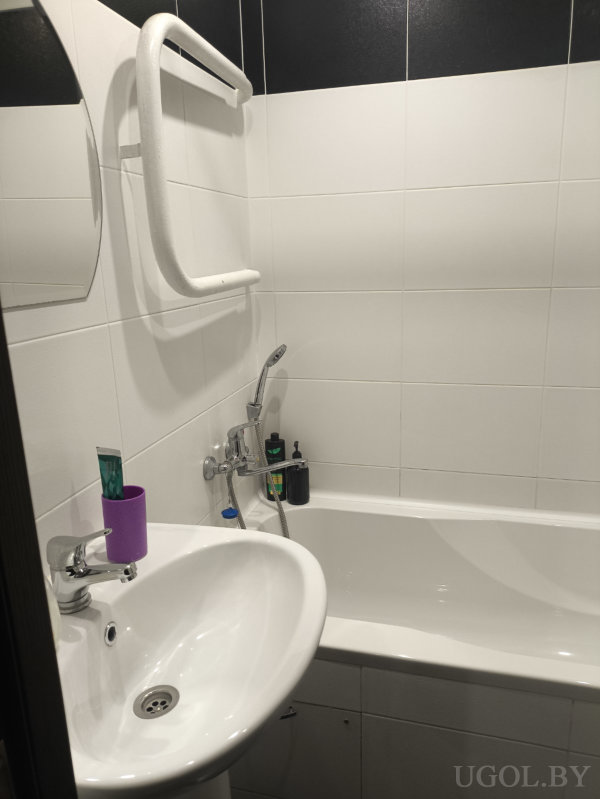 Раковина с пастой и щёткой, зеркало, полотенцесушитель и флаконы на бортике ванны.