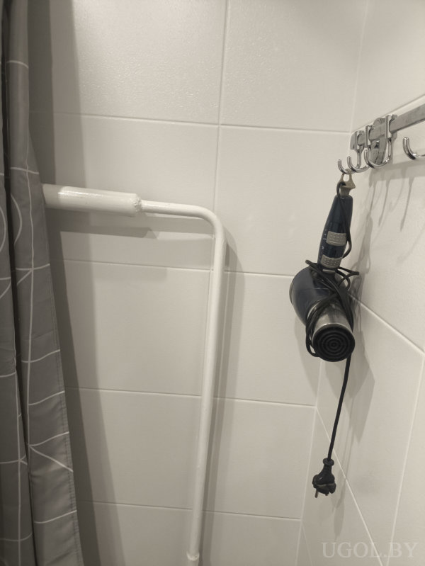 Серая штора, белая труба и фен, подвешенный на металлическом держателе.