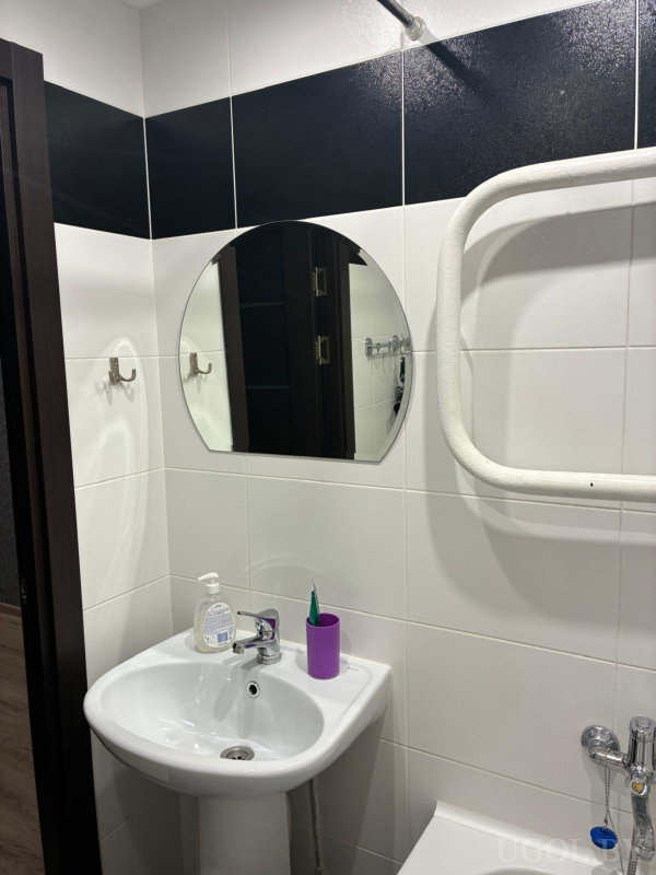 Раковина с аксессуарами, чёрная плитка, полотенцесушитель и сантехнические элементы.