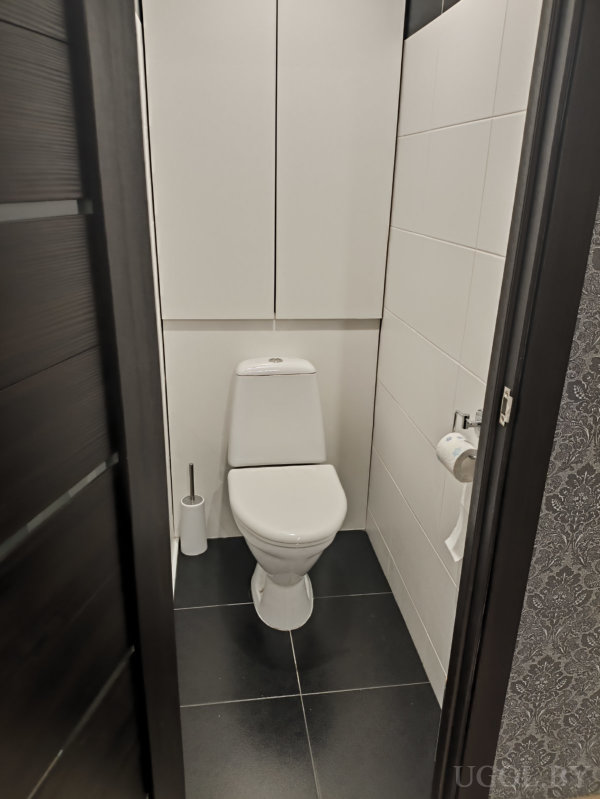 Компактный санузел с белым унитазом, шкафами, держателем бумаги и чёрной плиткой.