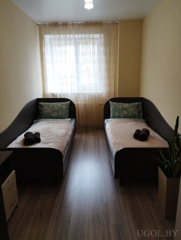 Небольшая спальня с двумя односпальными кроватями, белым бельём, коричневыми полотенцами и растением у окна.