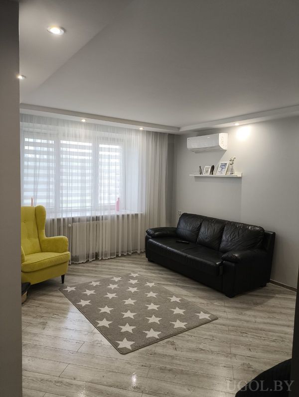 Современная гостиная с чёрным диваном, ярким жёлтым креслом, ковром со звёздами и полкой с фотографиями под кондиционером.