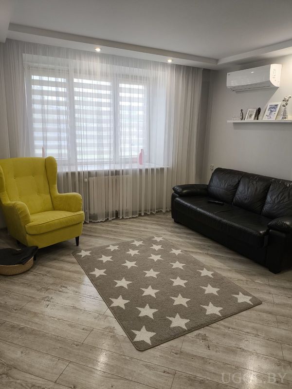 Уютная гостиная с жёлтым креслом, чёрным диваном, ковром со звёздами и полкой с фотографиями под кондиционером.