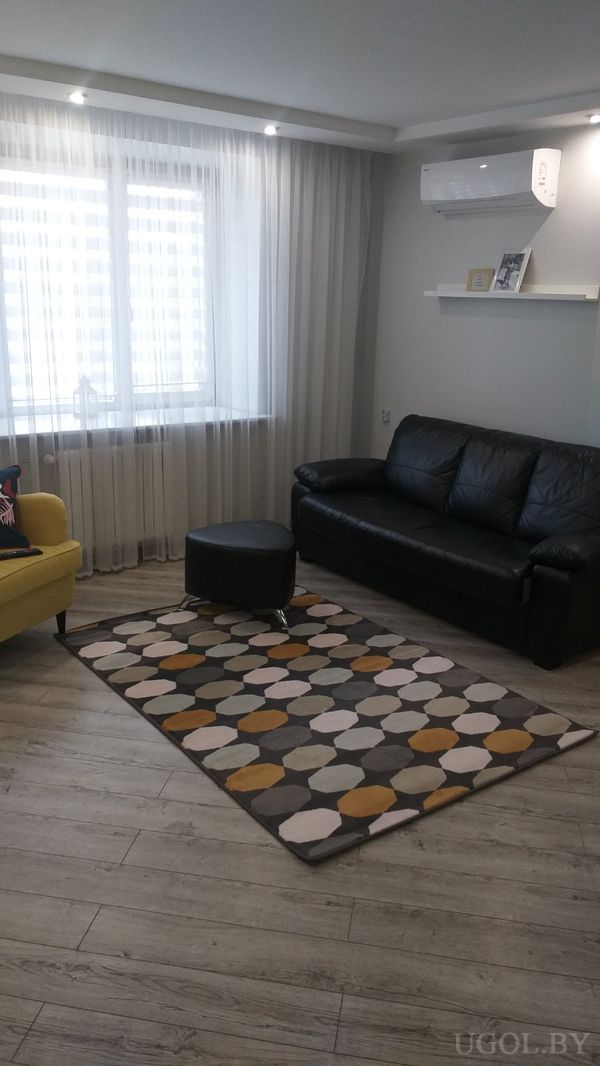 Комната с чёрным диваном, жёлтым креслом с подушкой Union Jack, круглым пуфом и ковром с геометрическим узором.