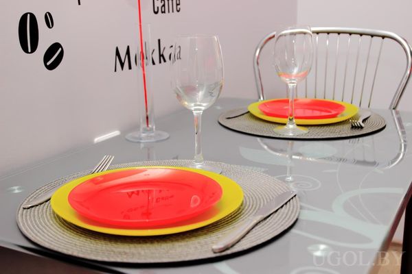 Современная столовая с круглым столом, сервированным на двоих яркими тарелками, бокалами и декоративной стеной с надписями.