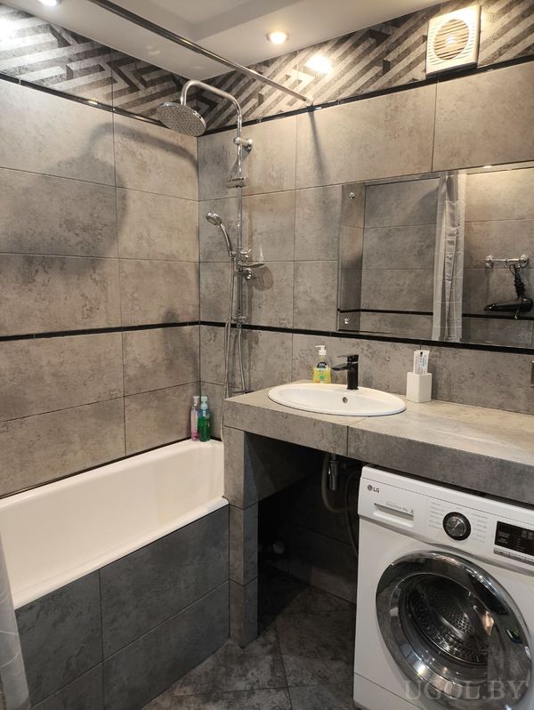 Современная ванная с белой ванной, серой плиткой, встроенной стиральной машиной LG и умывальником с зеркалом.