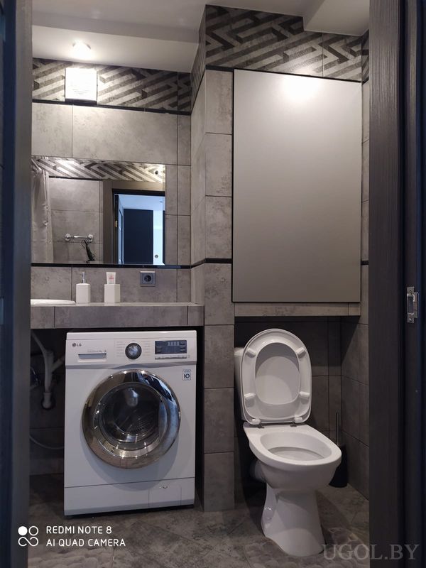 Компактная ванная с унитазом, стиральной машиной LG, умывальником с зеркалом и серой плиткой с узором.
