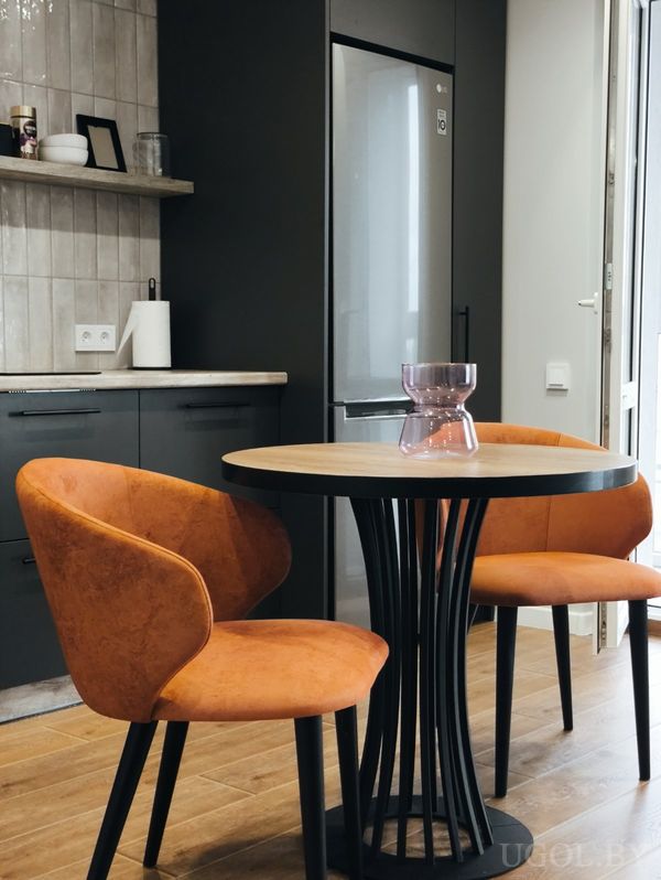 Компактная кухня с серыми шкафами, круглым столом с оранжевыми креслами и открытой дверью во двор.