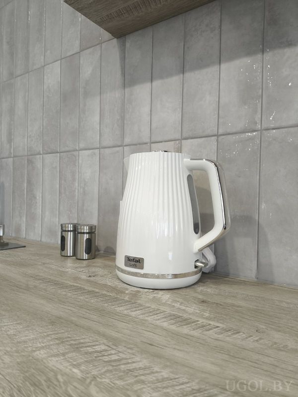 Фрагмент кухни с деревянной столешницей, белым электрическим чайником Tefal и металлическим контейнером.