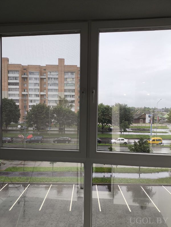 Городской вид из окна на улицу с машинами, жилыми домами и деревьями в дождливую погоду.