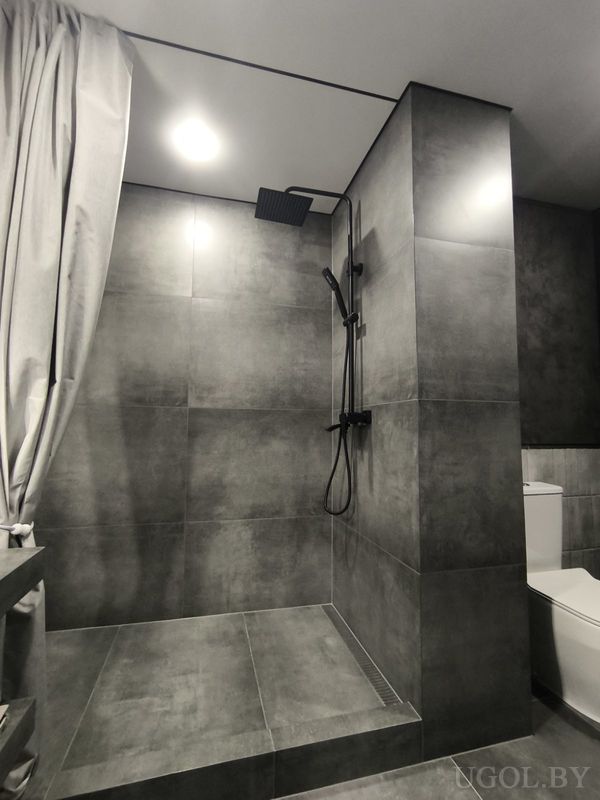 Современная ванная с душем, серой плиткой, белым унитазом и занавеской.