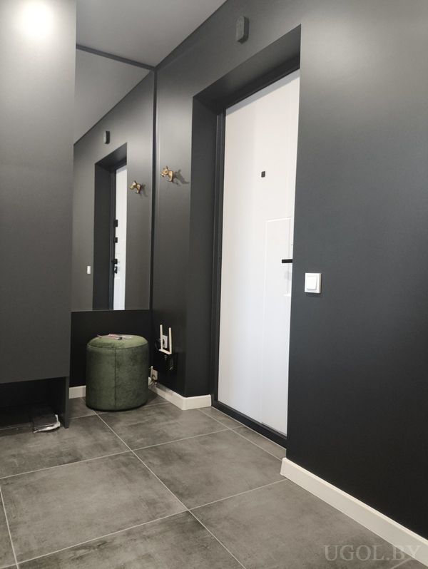 Уютная прихожая с зеркалом, зелёным пуфом, тёмной стеной и белой дверью.