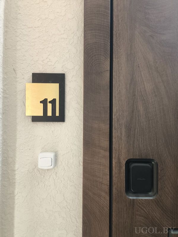 Тёмная деревянная дверь с номером 11, чёрной ручкой и кнопкой звонка на стене.