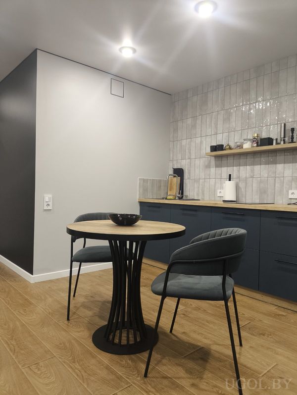 Современная кухня с тёмно‑синими шкафами, серым фартуком, деревянной столешницей и круглым столом с тёмными креслами.