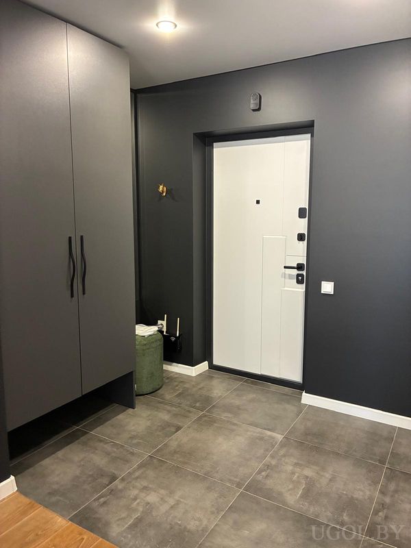 Уютная прихожая с белой дверью, высоким шкафом, зелёным пуфом и тёмной стеной.