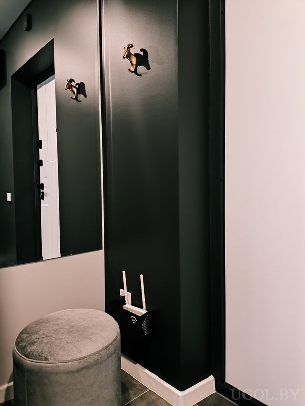 Интерьерная ниша с зеркалом, декоративными крючками‑животными, Wi‑Fi роутером и серым пуфом.