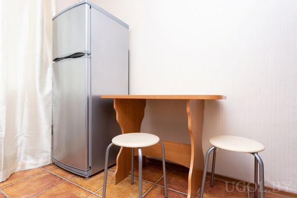 Компактная кухня с серебристым холодильником, деревянным столом и двумя табуретами.