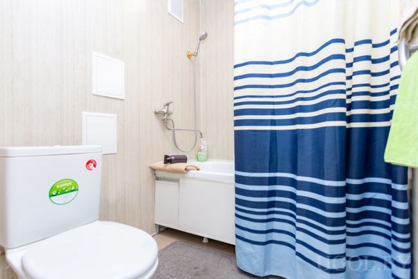 Небольшая ванная с белой ванной, душем, унитазом и голубой полосатой шторкой.