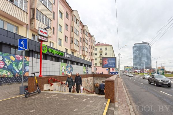 Городская улица с магазином Евроопт, подземным переходом и современным круглым зданием на фоне.