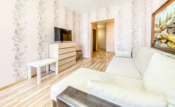 Интерьер с диваном, телевизором, тумбой, круглым столиком, картиной и проходом в коридор с глянцевым полом.