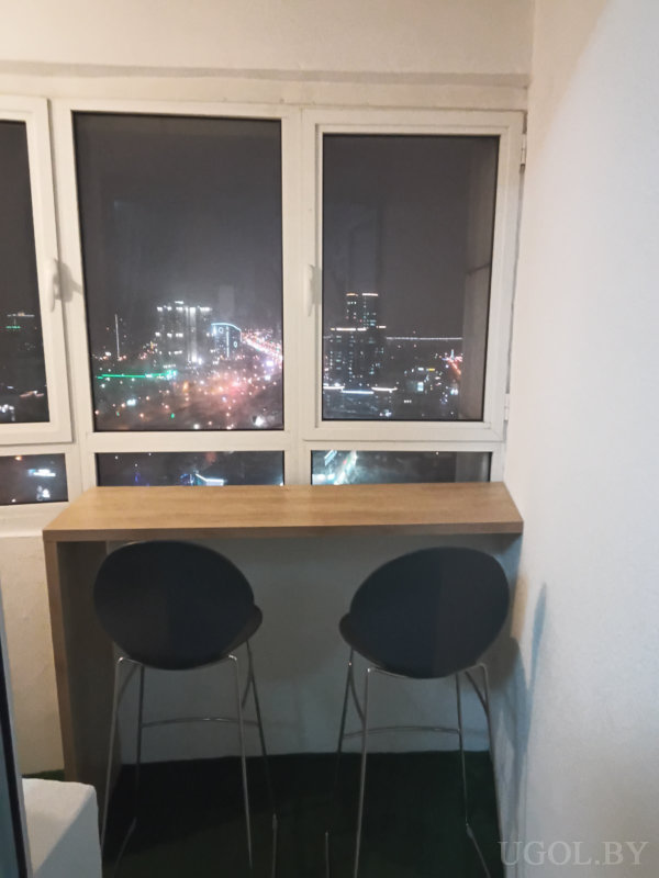 Застеклённая зона с барной стойкой, двумя стульями и ночным видом на город.