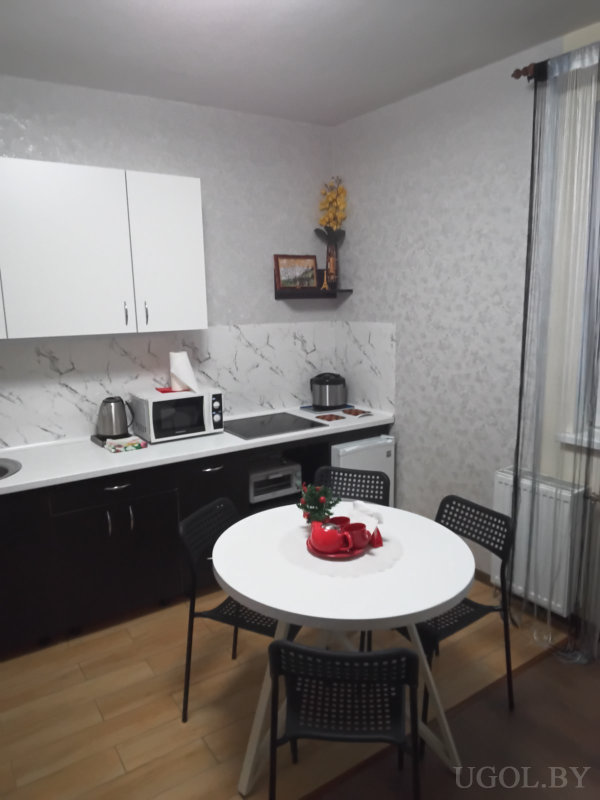 Интерьер с белыми верхними шкафами, чёрными нижними, круглым столом, чайным сервизом и полками с декором.