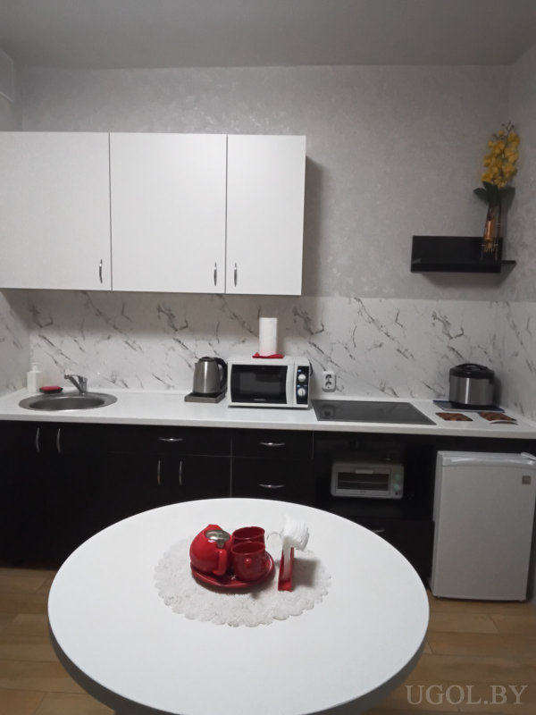 Рабочая зона с техникой, белыми шкафами, чайным сервизом на столе и вазой с цветами на полке.