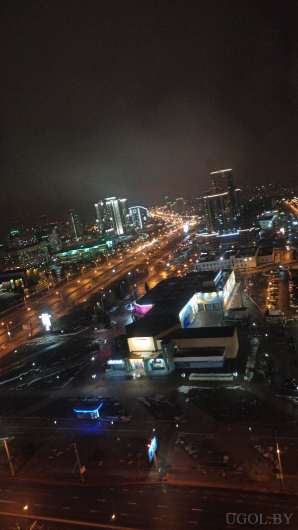 Панорама с освещёнными зданиями, дорогами, торговым центром и архитектурной подсветкой.