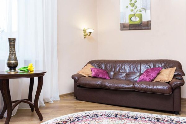 Часть гостиной с коричневым диваном, подушками, круглым столиком с вазой тюльпанов и картиной на стене.