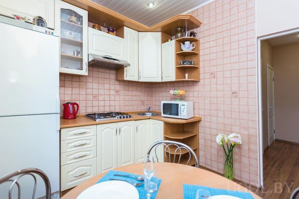 Компактная кухня с кремовыми шкафами, плитой, холодильником и круглым столом, сервированным посудой и цветами.