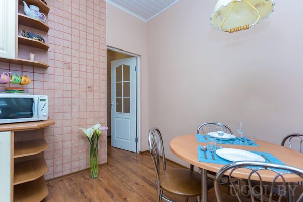 Кухня с круглым столом, сервированным на троих, белыми шкафами, микроволновкой и вазой с каллами.