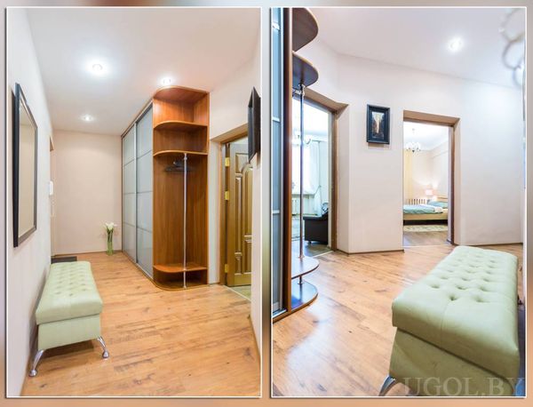 Светлый коридор с деревянным полом, зелёной мягкой скамьёй, зеркалом и вазой с белыми цветами у двери.