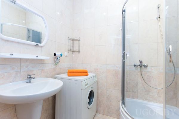 Компактная ванная с угловой душевой кабиной, стиральной машиной с оранжевыми полотенцами и раковиной с зеркалом.