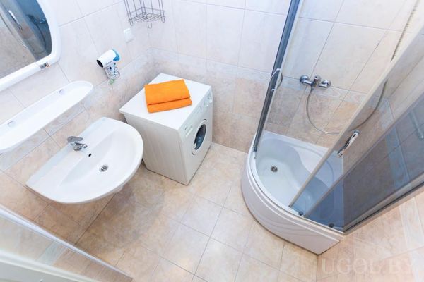 Светлая ванная с душевой кабиной, стиральной машиной с полотенцами, раковиной и светлой плиткой.