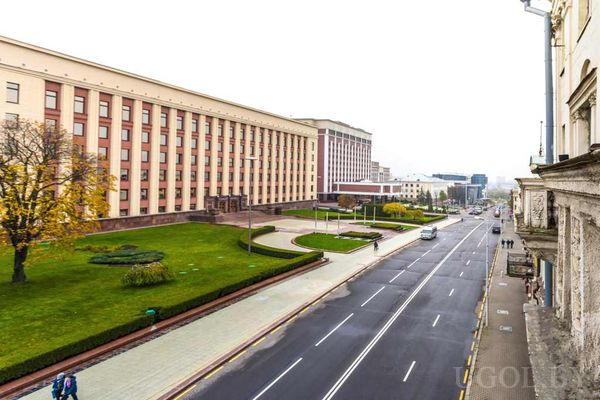 Широкая улица с административными зданиями, зелёными газонами и осенними деревьями.